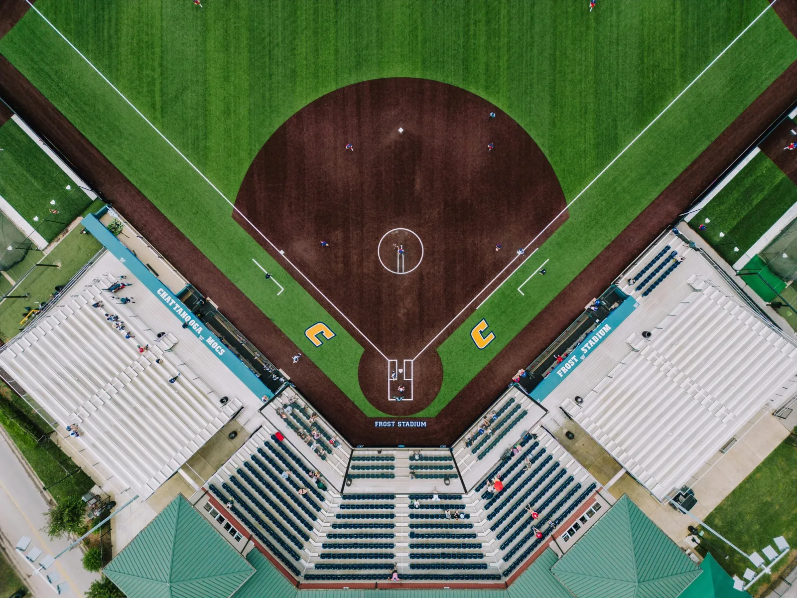 A college softball field with green grass, dirt infield, and stadium seating