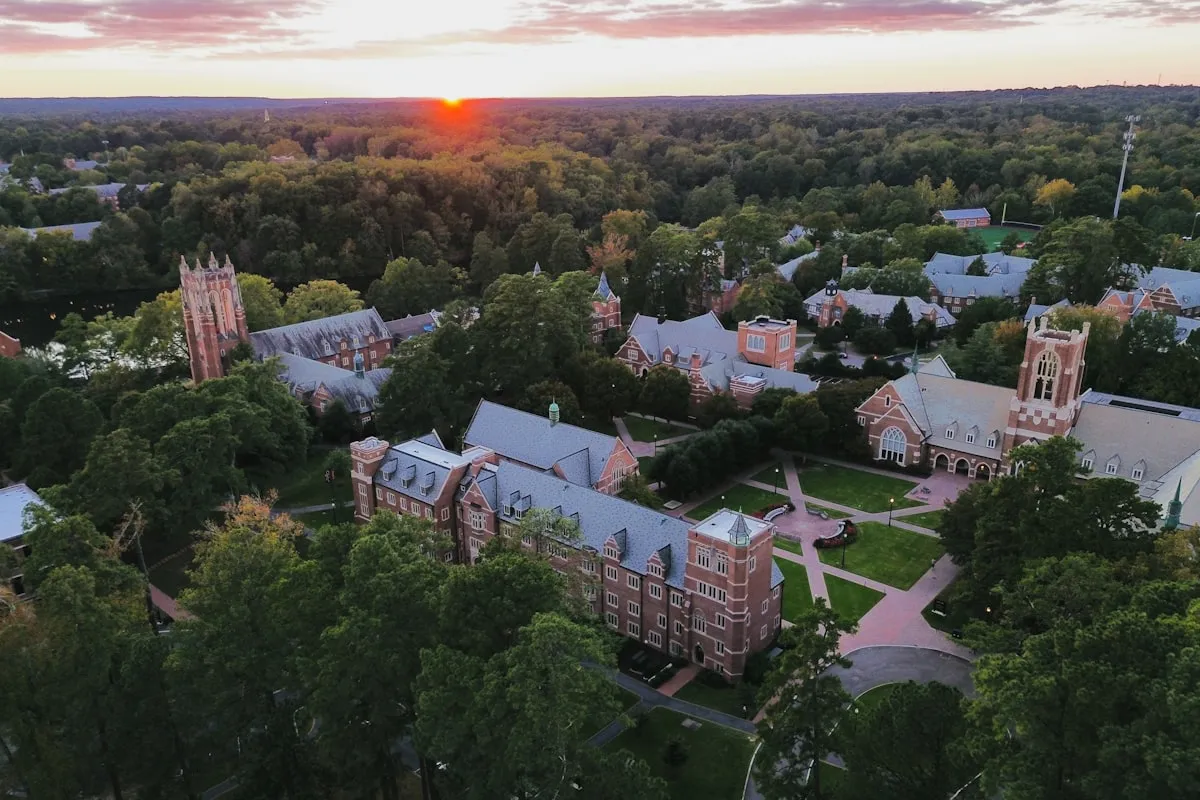 Aerial view of a university campus at sunset with Gothic brick buildings and tree-lined pathways