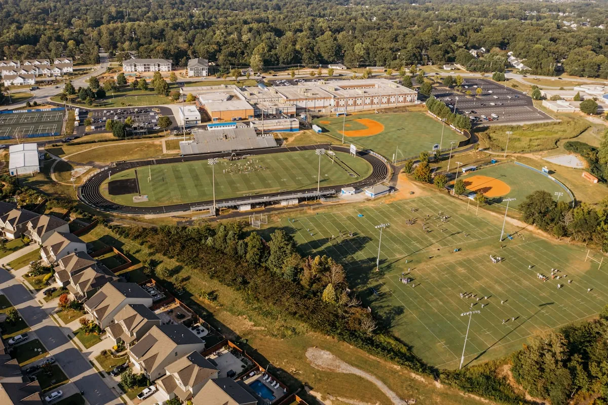 Aerial view of a school campus with multiple athletic fields and athletes practicing in warm afternoon light