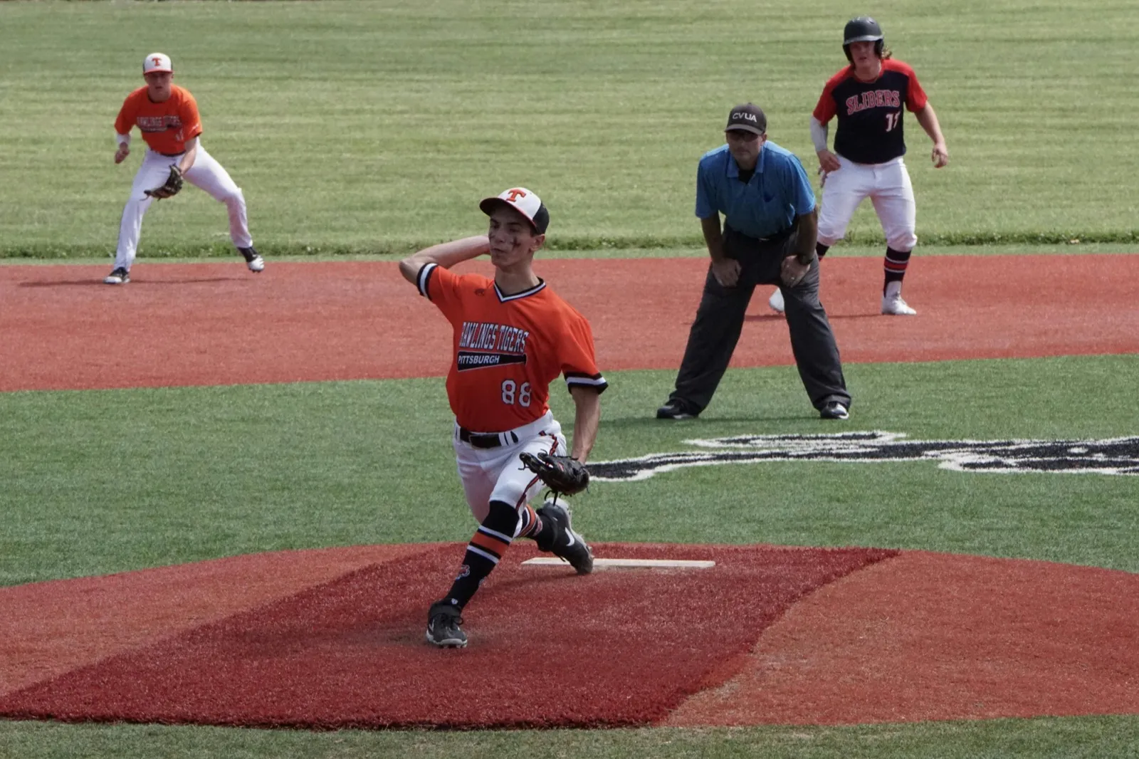 A baseball pitcher in an orange jersey starting his delivery on the mound
