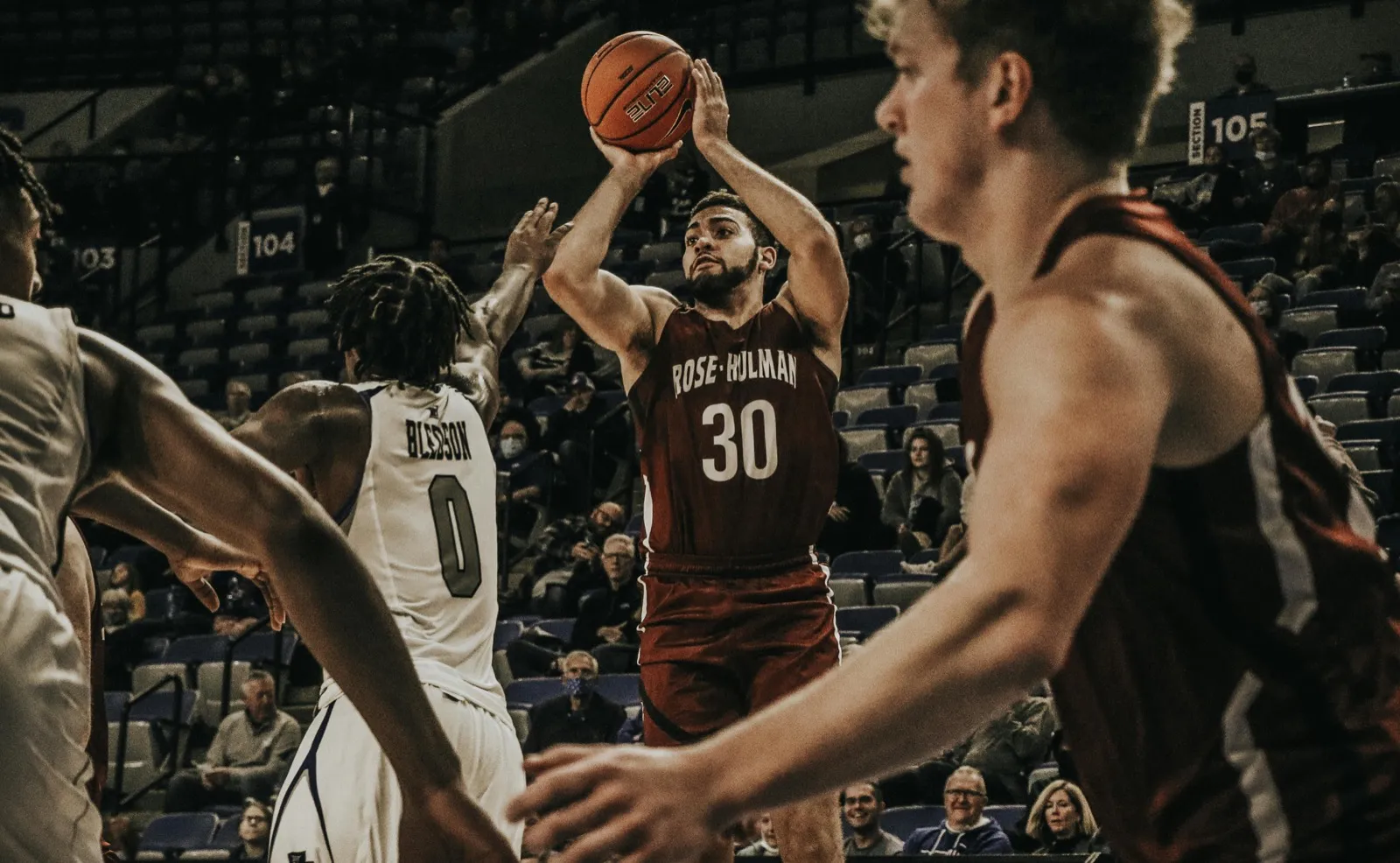A basketball player taking a jump shot in a college-style arena
