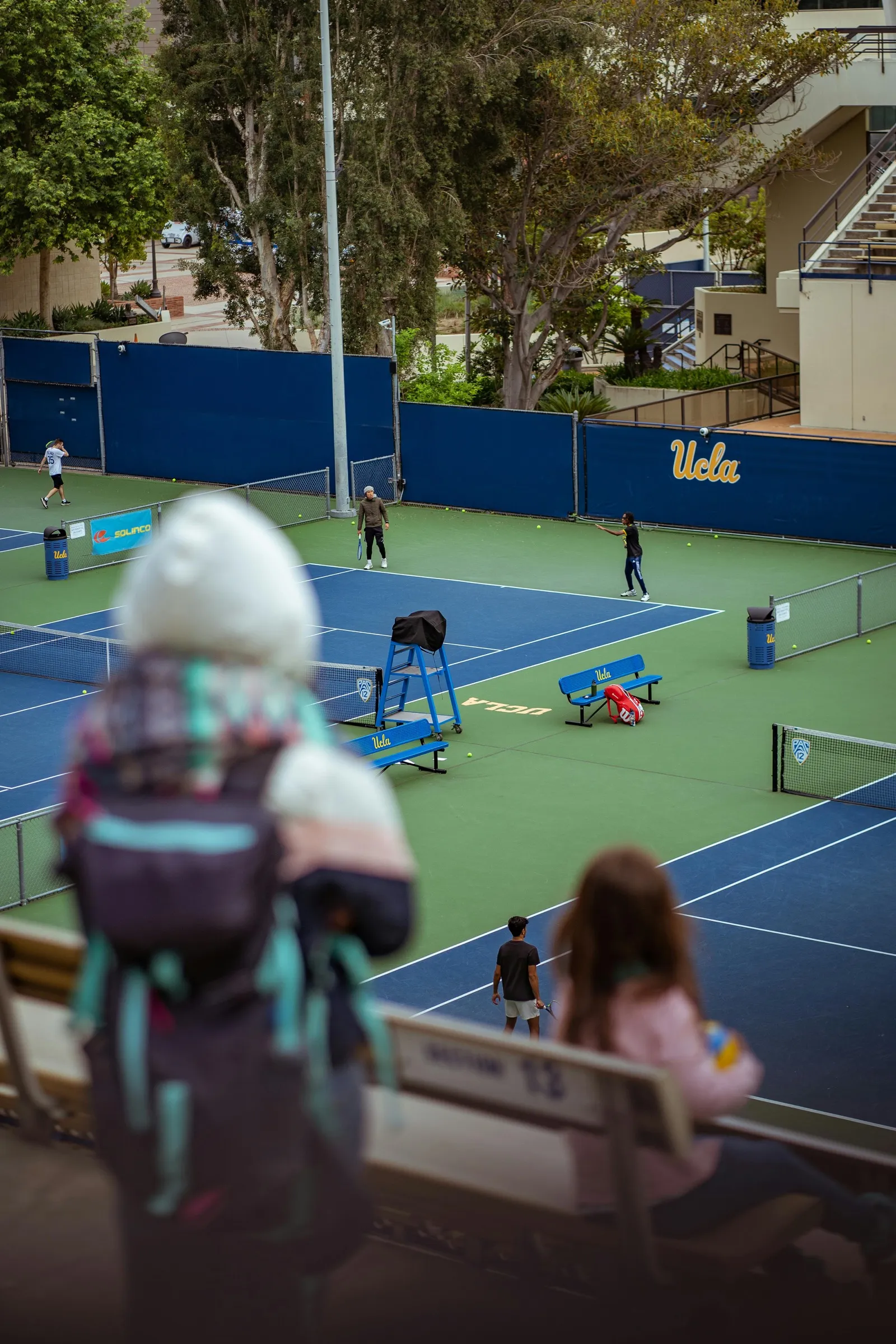 College tennis courts with fans watching a match