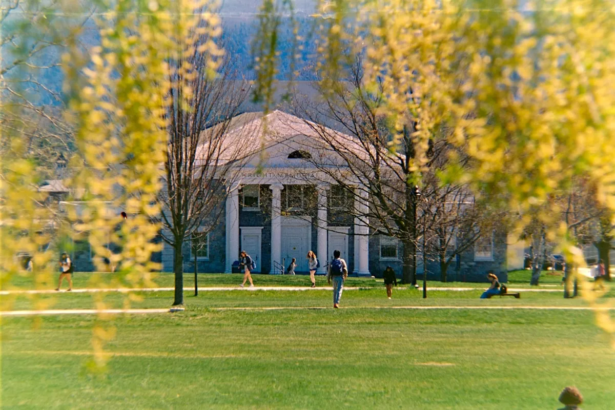 Students walking across a college campus quad toward a columned academic building