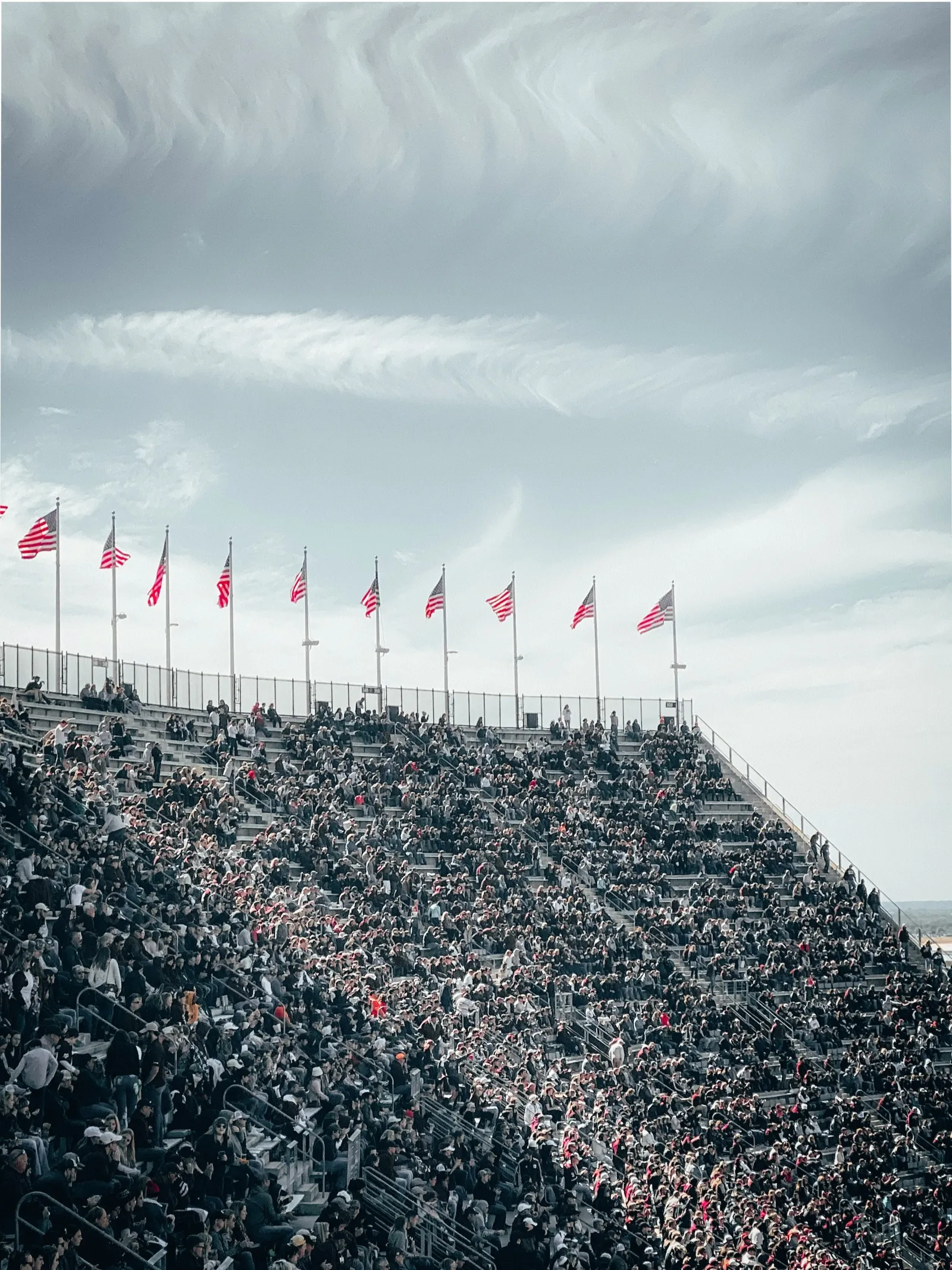 Packed stadium stands with fans holding American flags at a college athletic event
