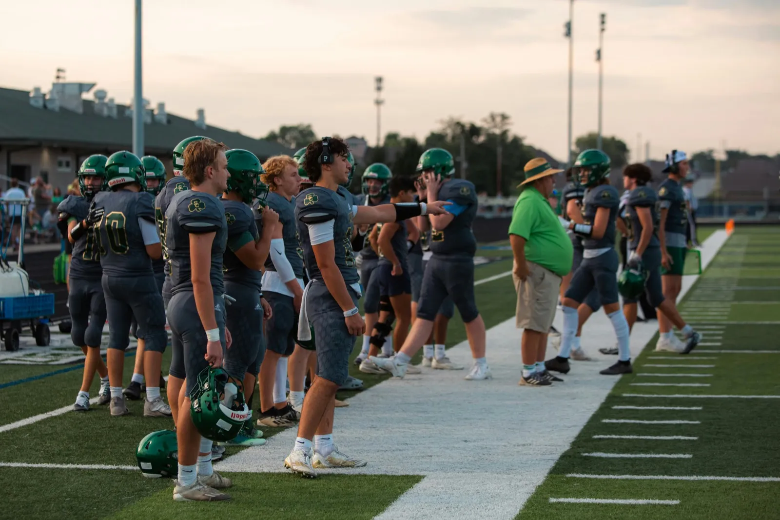 Football players in green helmets standing on the sideline during a game
