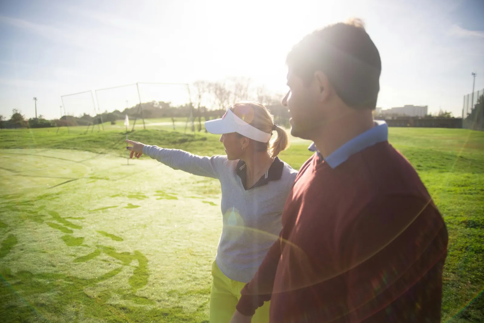 A golf coach pointing while speaking to a player at a driving range during sunset