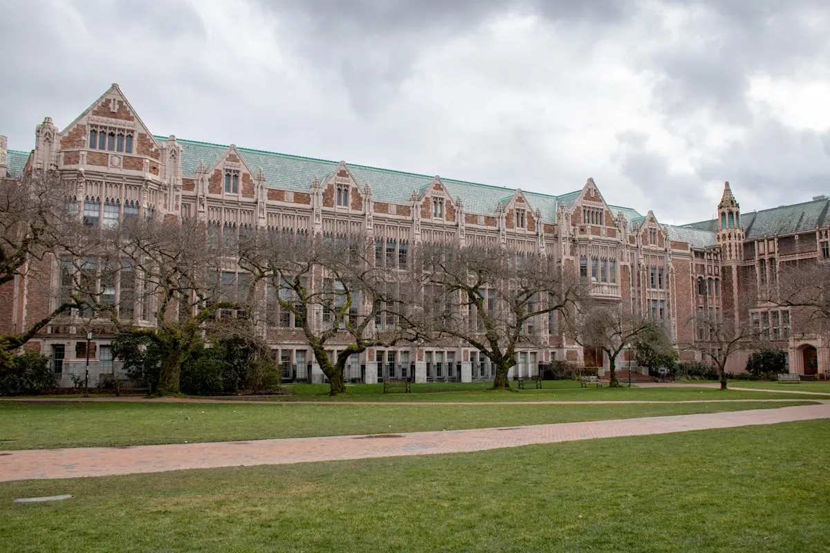 A stately Gothic-style college campus building with green copper roof and bare trees on a cloudy day