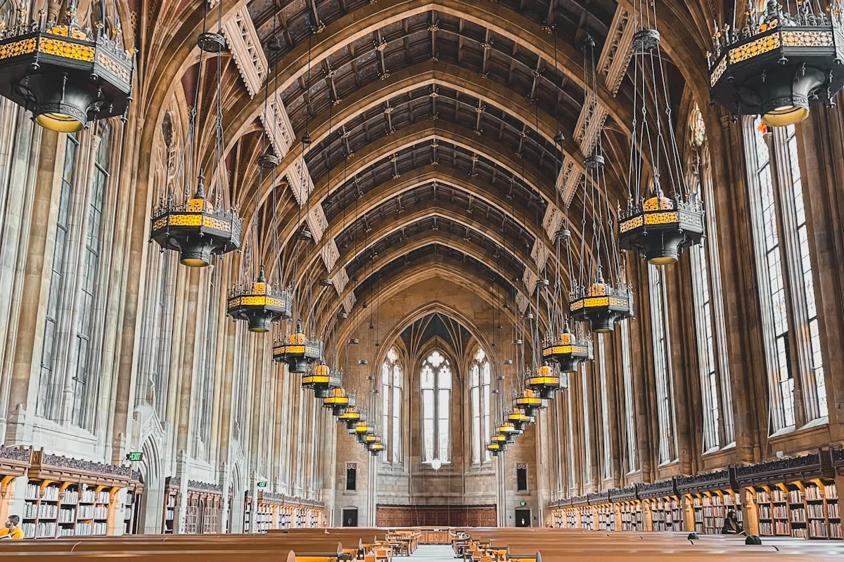 Interior of a grand collegiate library with Gothic arched ceilings, long wooden reading tables, and rows of bookshelves