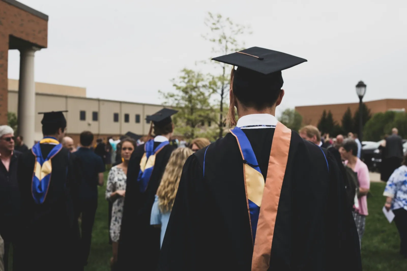 College graduates in caps and gowns gathered on a campus lawn at a commencement ceremony
