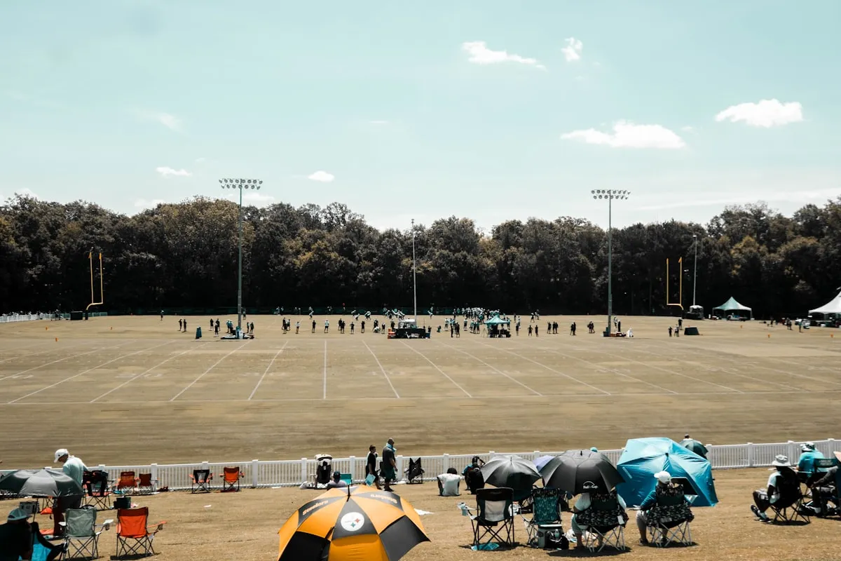 Wide view of a sports practice field with athletes training and spectators watching from the sideline