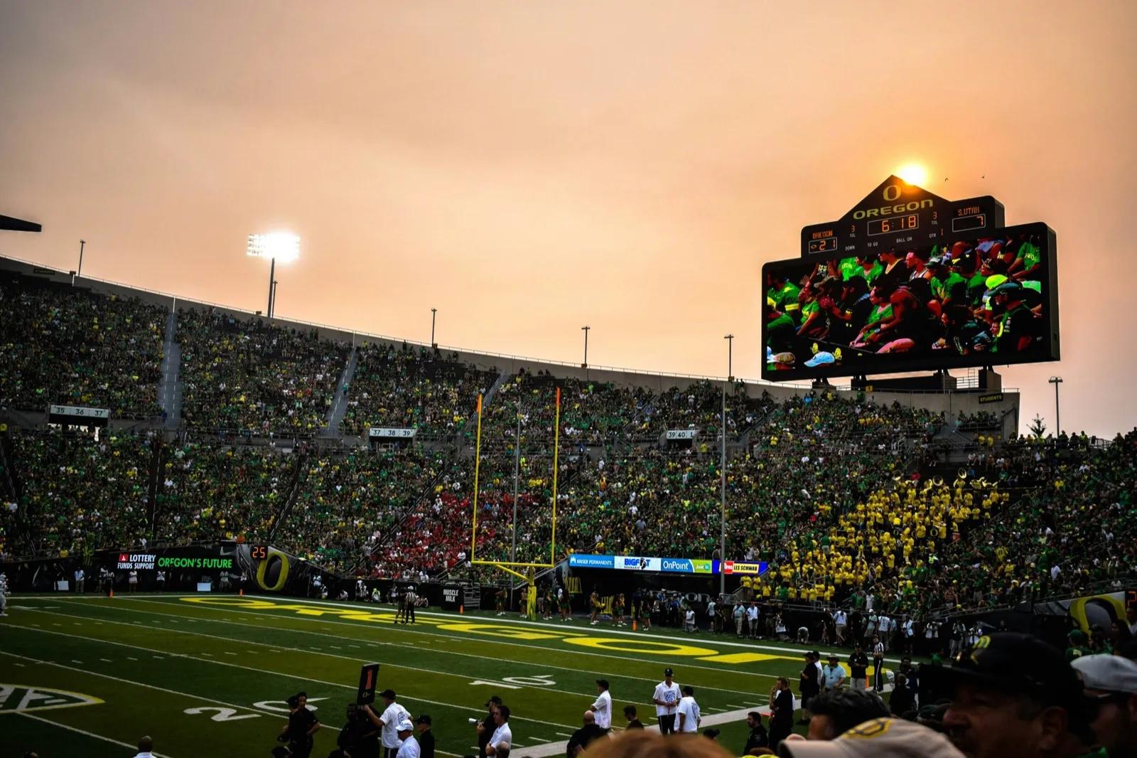 A college football stadium at dusk with the lights on and fans filling the stands