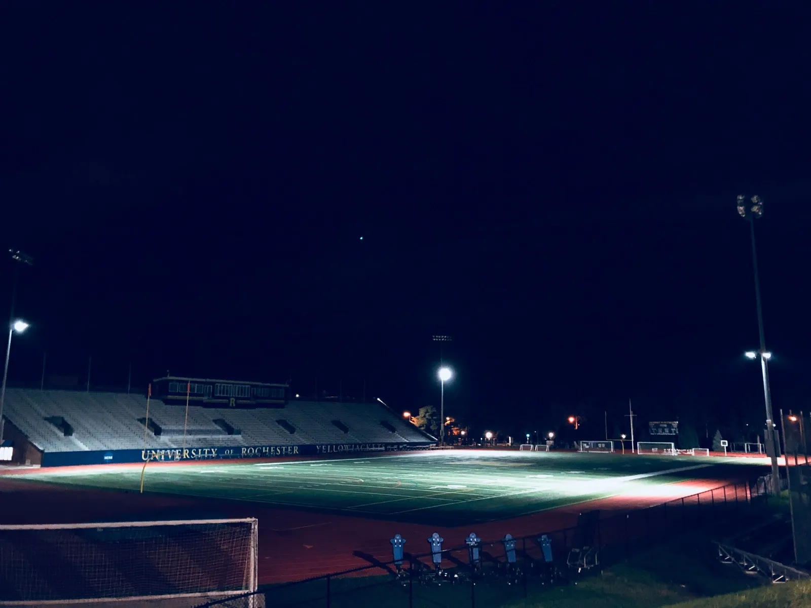 A college athletic field lit at night with stadium lights reflecting off the artificial turf surface