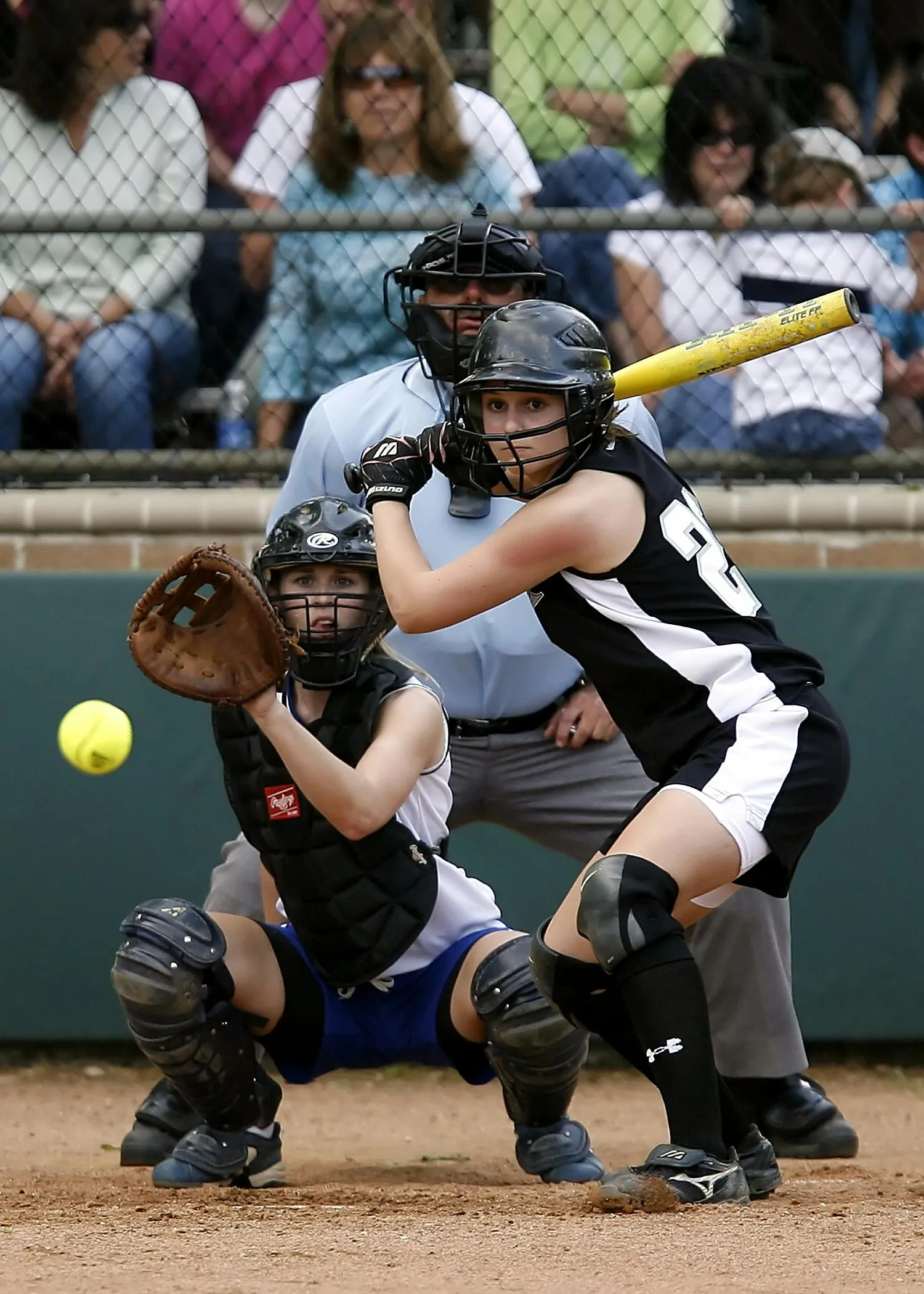 A softball batter at the plate with a catcher and umpire behind her
