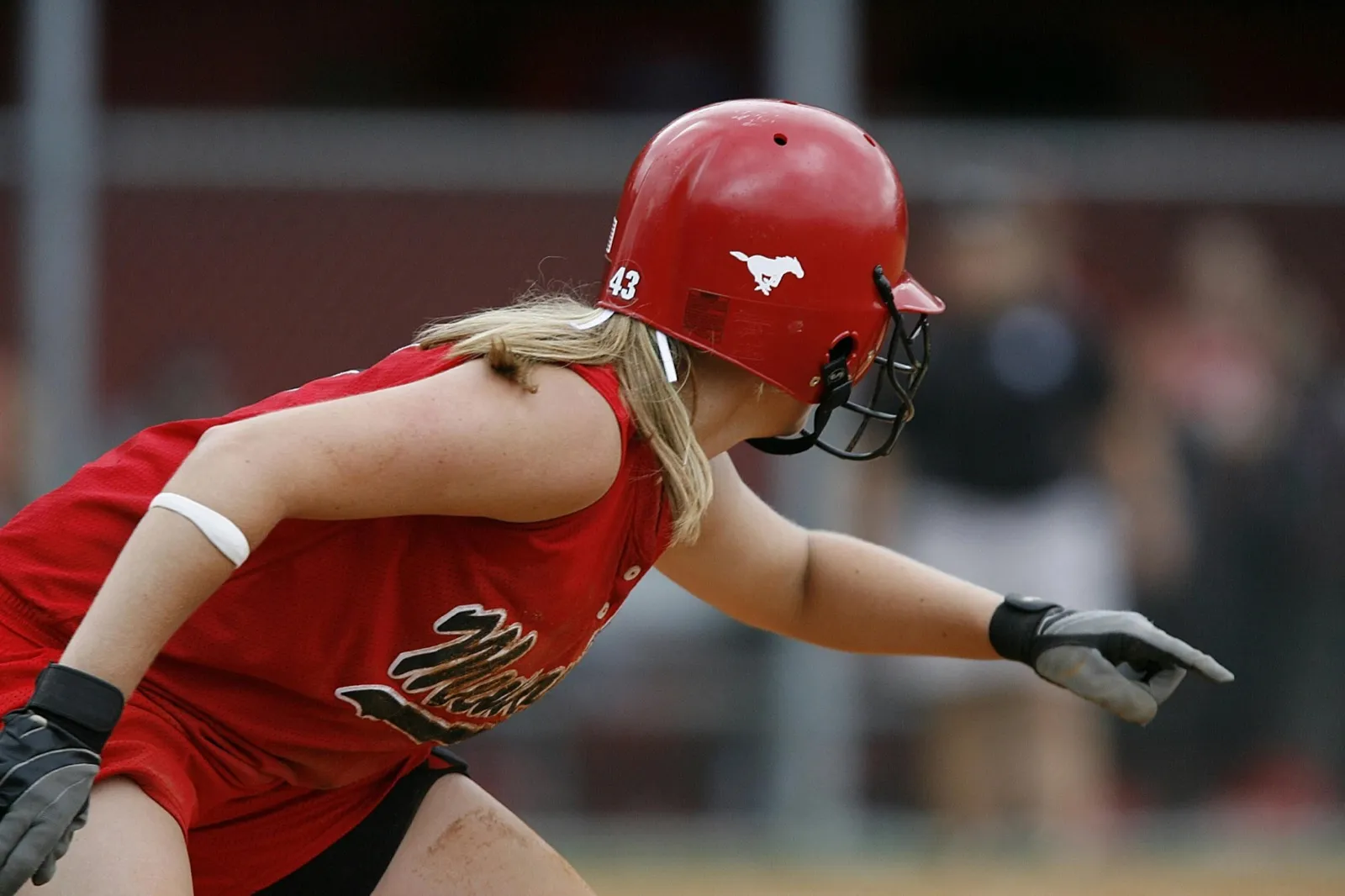 A softball player in a red helmet sprinting out of the batter's box during game action