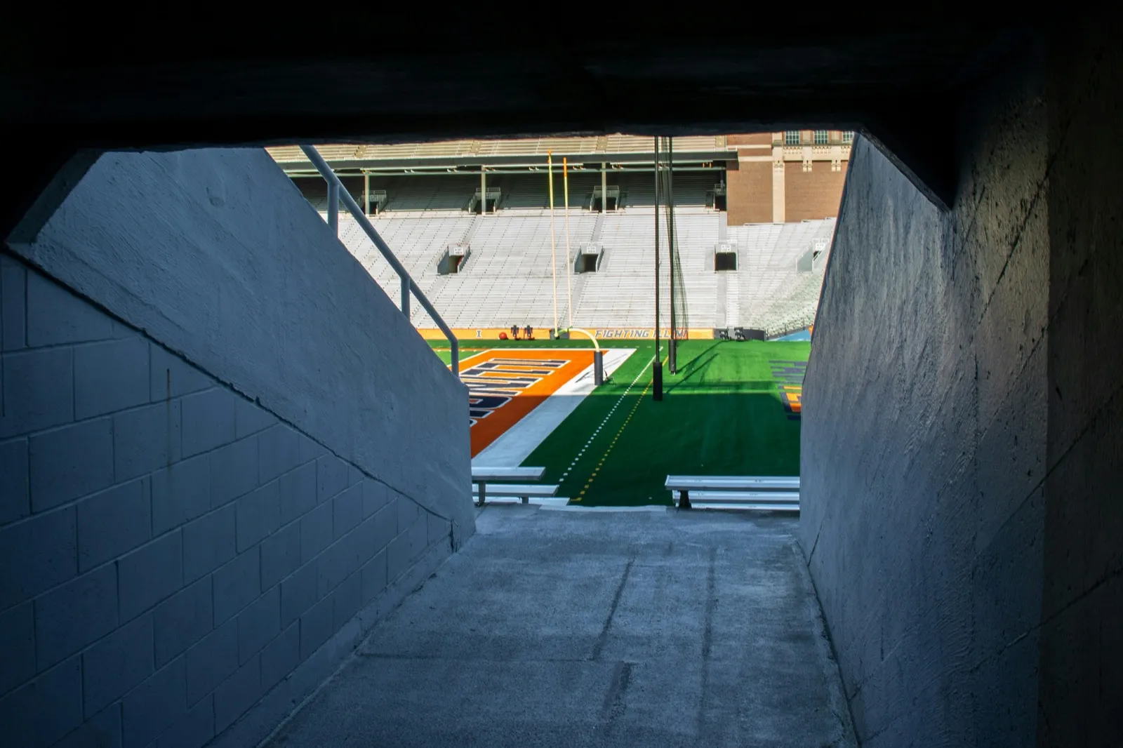 View through a stadium tunnel looking out onto an empty college football field with goalpost and stadium seating visible