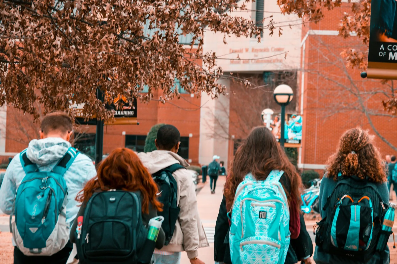 A group of students walking together on a college campus with fall foliage visible in the background