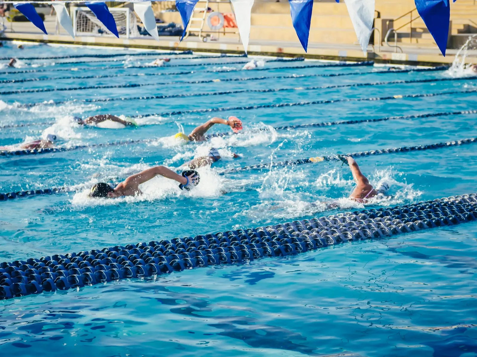 Swimmers racing freestyle in an outdoor pool with multiple lane dividers