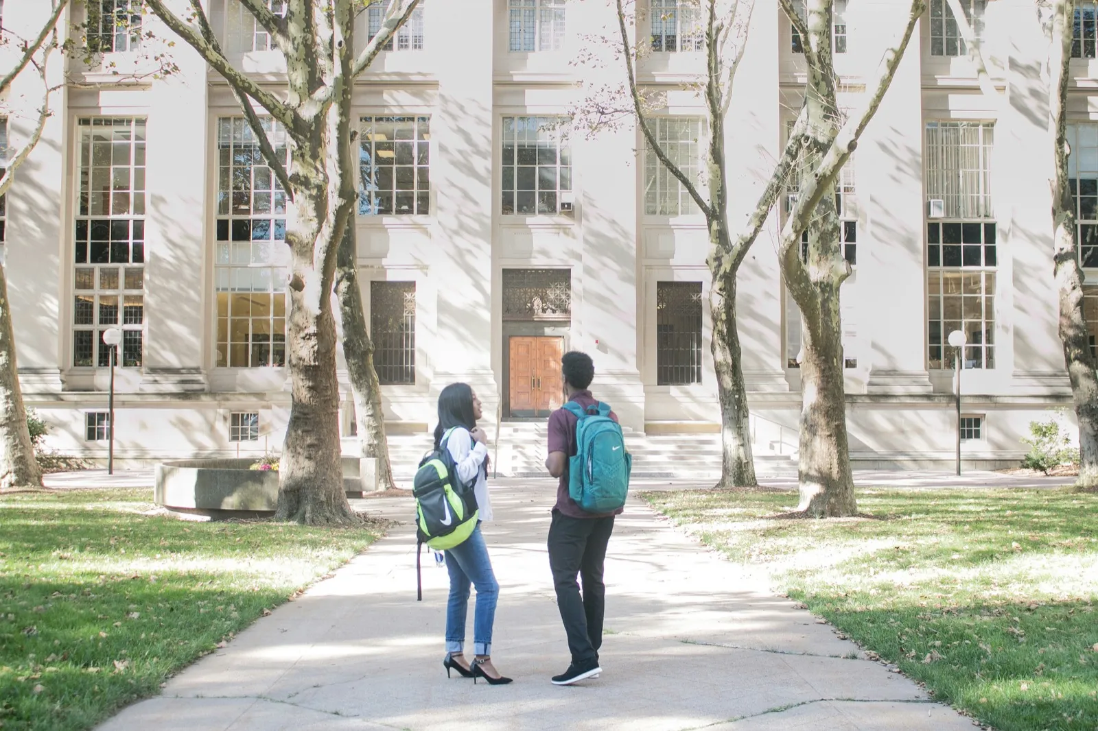 Two students walking together on a college campus carrying backpacks and talking